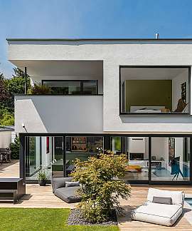 Modernes zweistöckiges Haus mit Terrasse, Pool und großer Glasfront im Garten.