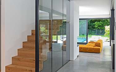 Modernes Interieur mit Holztreppe, Glaswänden und gelbem Sofa am Poolblick.