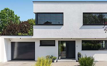 Modernes weißes Haus mit dunklen Fenstern, Garage und Vorgarten.