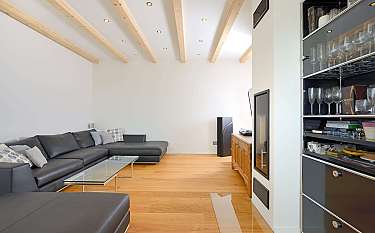 Helles Wohnzimmer mit schwarzem Ecksofa, Holzboden und Glasvitrine.