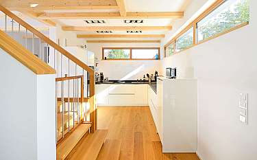 Helle moderne Küche mit Holzdecke, großen Fenstern und Treppe im Vordergrund.