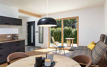 Helles modernes Wohn-Esszimmer mit Küchenzeile, Sofa, Esstisch und großer Glasfront zum Garten.