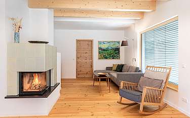 Helles Wohnzimmer mit Kamin, Sofa, Schaukelstuhl und Holzbalkendecke.