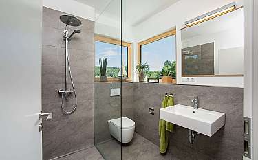 Modernes Badezimmer mit Glasdusche, Waschtisch und großen Fenstern.