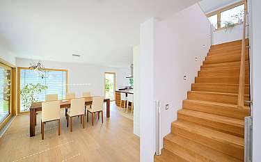 Moderner heller Wohn- und Essbereich mit Holztreppe, Esstisch und großen Fenstern.