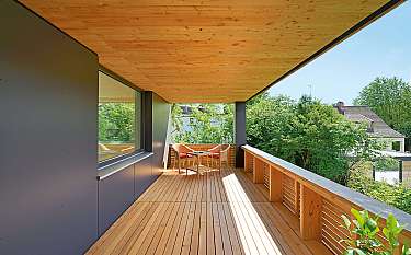 Überdachter Holzbalkon mit zwei Stühlen, Tisch und Blick ins Grüne.