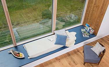 Helle Fensterbank mit Kissen, Büchern und Blick ins grüne Außenareal.
