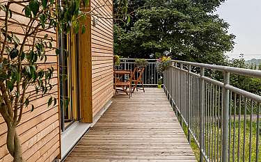 Holzterrasse neben einem modernen Holzhaus mit Geländer, Stühlen und Pflanzen