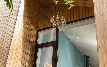 Moderne Holzwand mit Fenster und hängendem Kronleuchter unter einem überdachten Eingang.