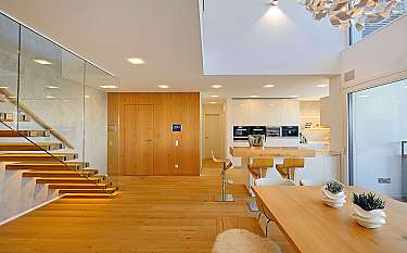 Modernes, helles Wohn-Esszimmer mit offener Küche, Holztreppe und großem Oberlicht.