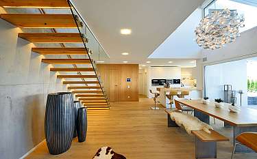 Modernes Interieur mit Holztreppe, Esstisch, Küche und großer Pendelleuchte.
