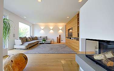 Helles, modernes Wohnzimmer mit Sofa, Holzwand, großem Teppich und Kamin im Vordergrund.