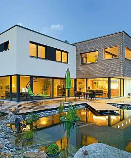 Modernes zweigeschossiges Haus mit beleuchteter Terrasse und Garten-Teich