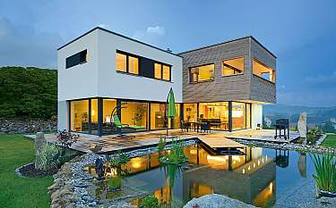 Moderne zweistöckige Villa mit beleuchteter Terrasse und Gartenteich.