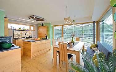 Helle moderne Küche mit Holzmöbeln, Esstisch und großen Fenstern mit Jalousien.