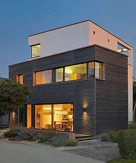 Modernes zweigeschossiges Haus mit großen Fenstern und warm erleuchteter Fassade.