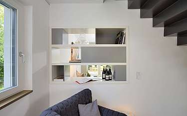 Helle Wohnzimmerecke mit Regalsystem, Fenster und dunkler Treppe.